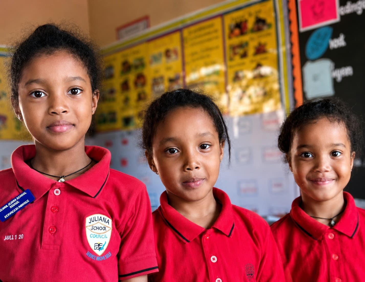 Three schoolgirls in uniform standing together in their classroom in Uganda