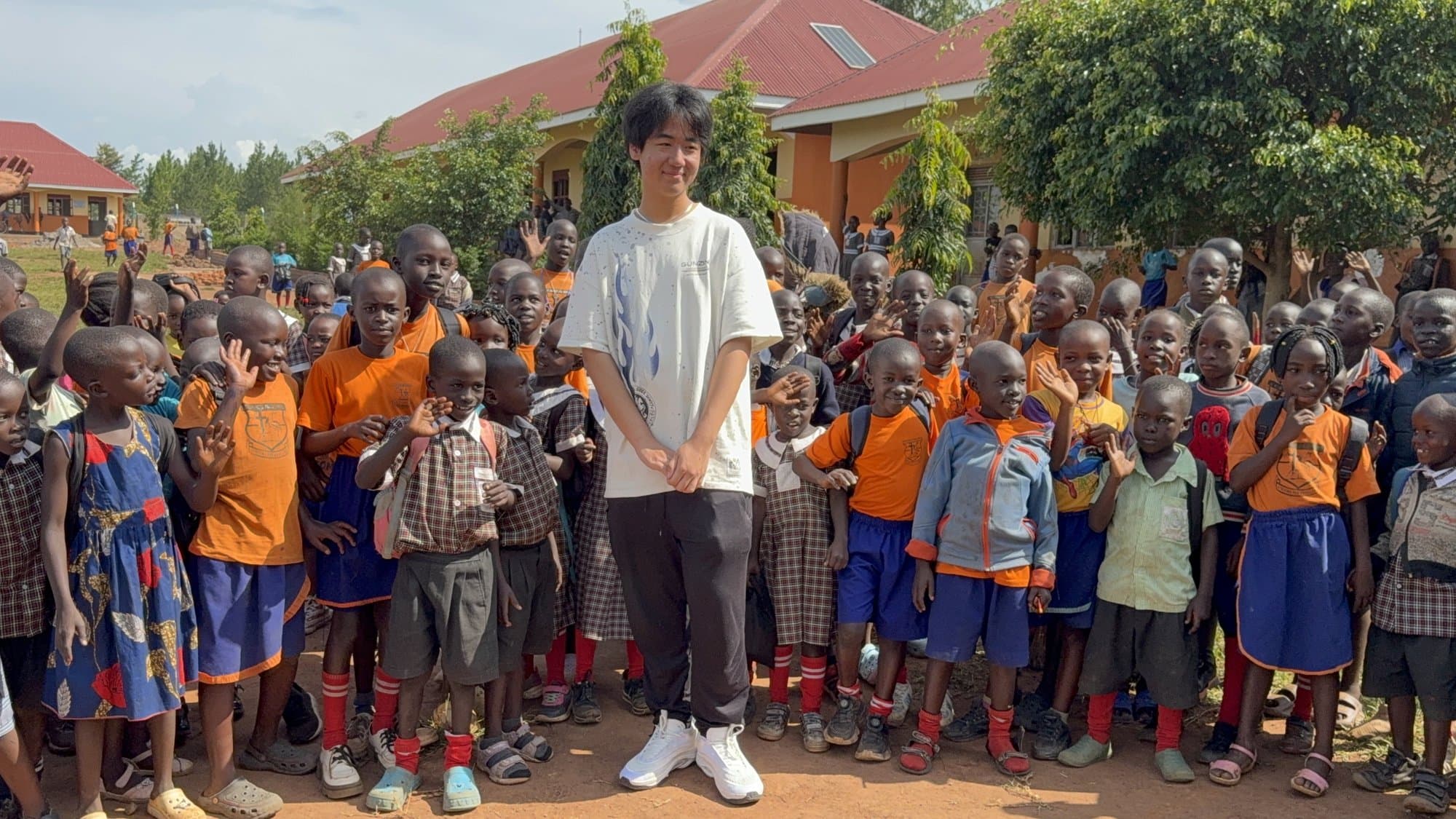 Eric Wang with a large group of schoolchildren and educators outside a school in Uganda